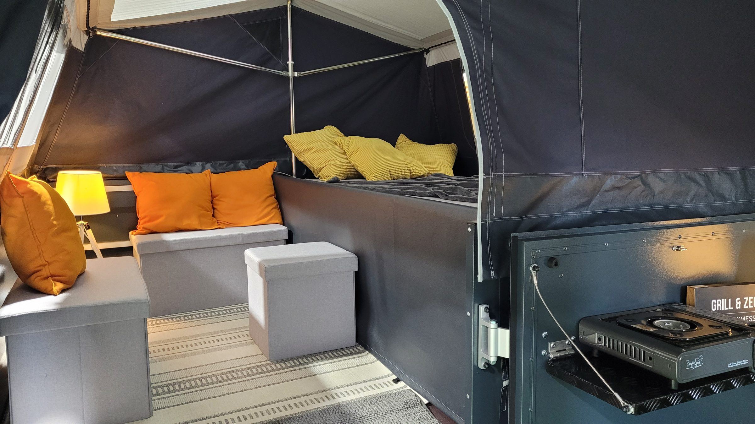 Wohnbereich im Klappcamper mit Kissen und Kocher