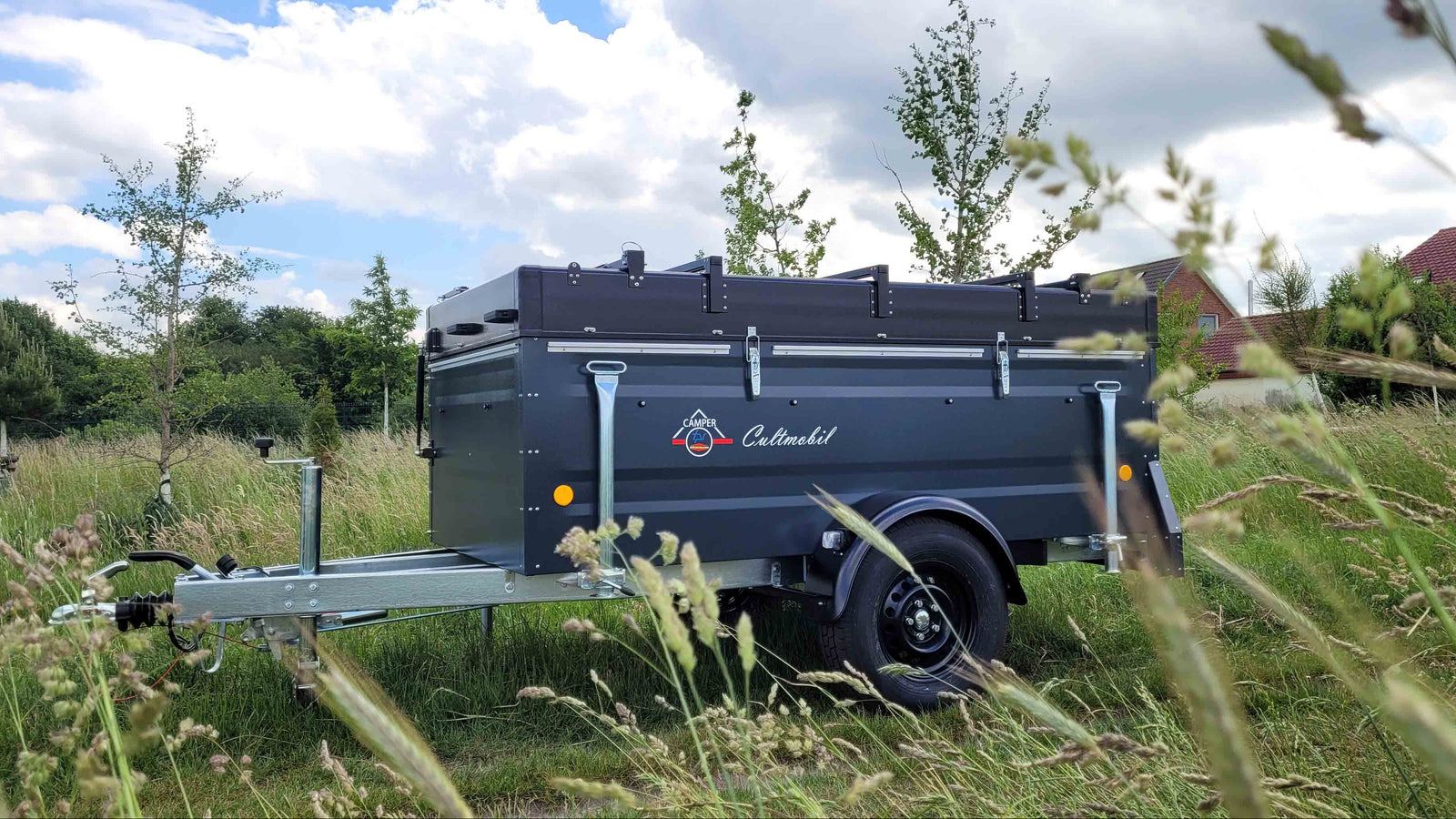 Es wird ein Faltcaravan auf einer Wiese in einer Siedlung gezeigt