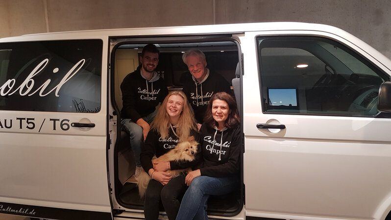 Das Cultmobil-Team mit Hund in der offenen Schiebetür eines VW-Busses
